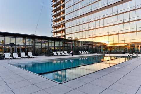 A large swimming pool is surrounded by lounge chairs in front of a modern building.