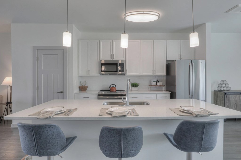 A modern kitchen with a white island and grey chairs.