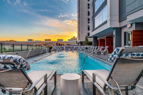 A pool area with lounge chairs and a view of the city skyline at sunset.
