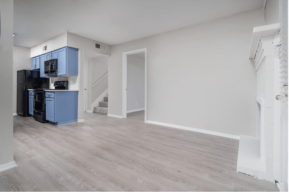 the living room and kitchen of an apartment with white walls and wood floors