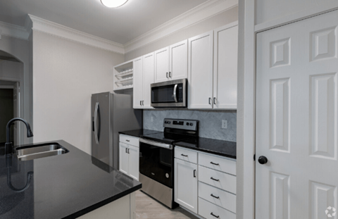 A kitchen with white cabinets and a black countertop.