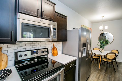A kitchen with a stove, oven, microwave, refrigerator, and a dining table with chairs.