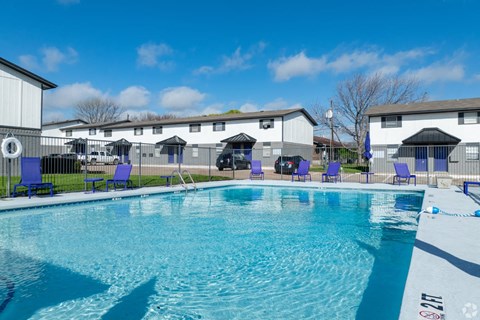 A swimming pool with blue chairs and a white building in the background.