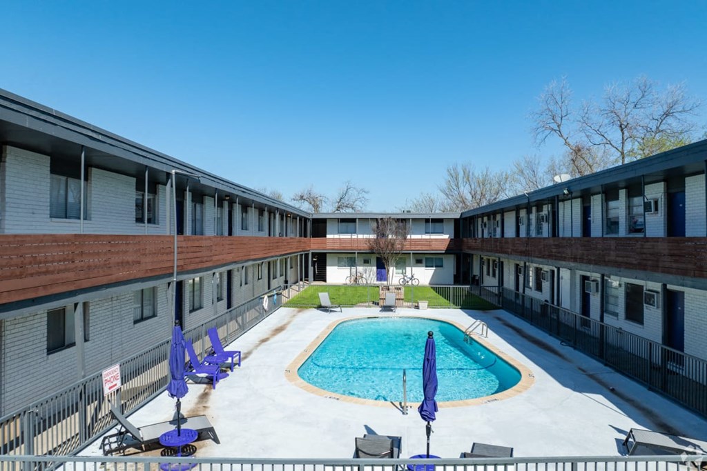A pool surrounded by lounge chairs and umbrellas in a sunny courtyard.