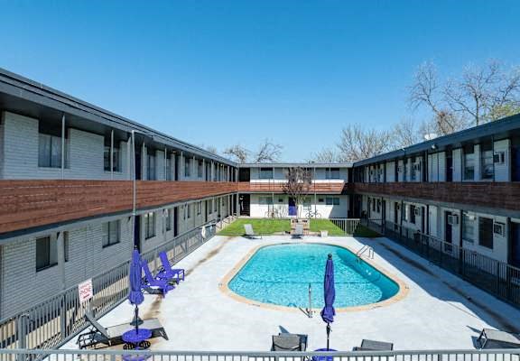 A pool surrounded by chairs and umbrellas in a courtyard.