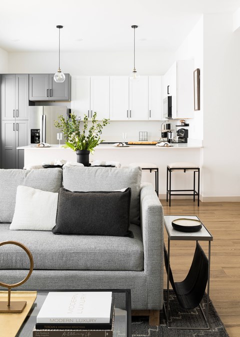 A grey couch with a black pillow and a vase with flowers on a coffee table.