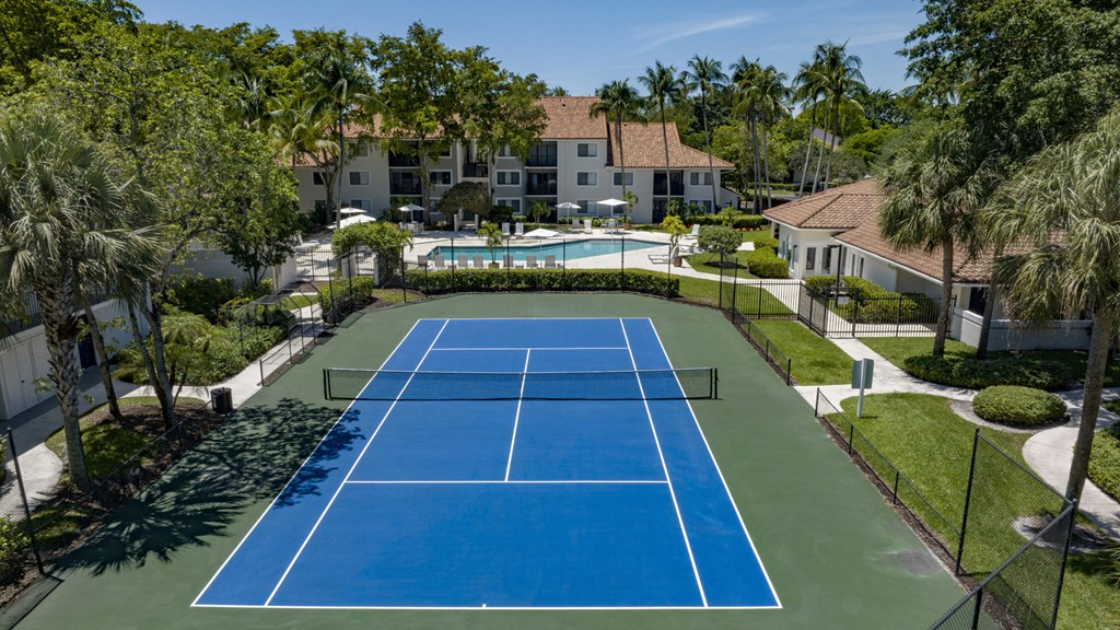 an aerial view of a tennis court with a pool and villas in the background
