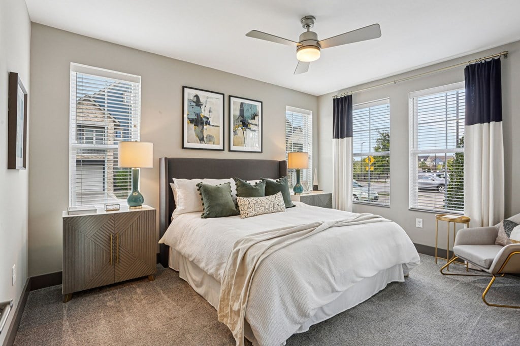 A bedroom with a large bed, a ceiling fan, and two lamps.