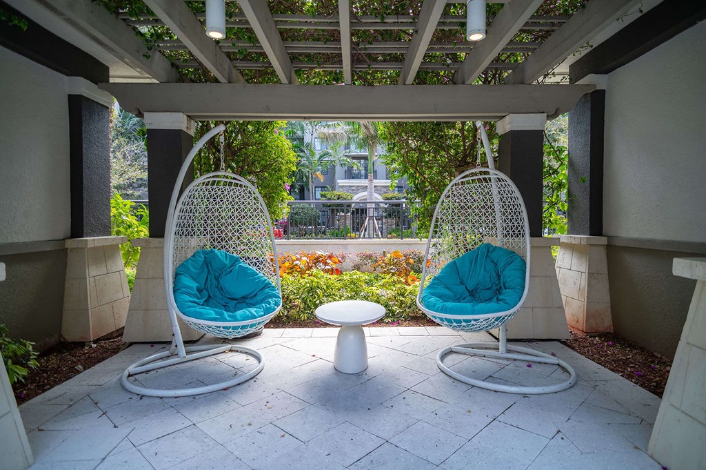 two hanging hammocks in a patio with a table and a garden