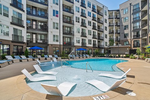 A swimming pool surrounded by lounge chairs in front of apartment buildings.