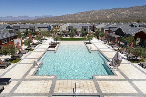 A large swimming pool surrounded by lounge chairs and umbrellas in a residential area.