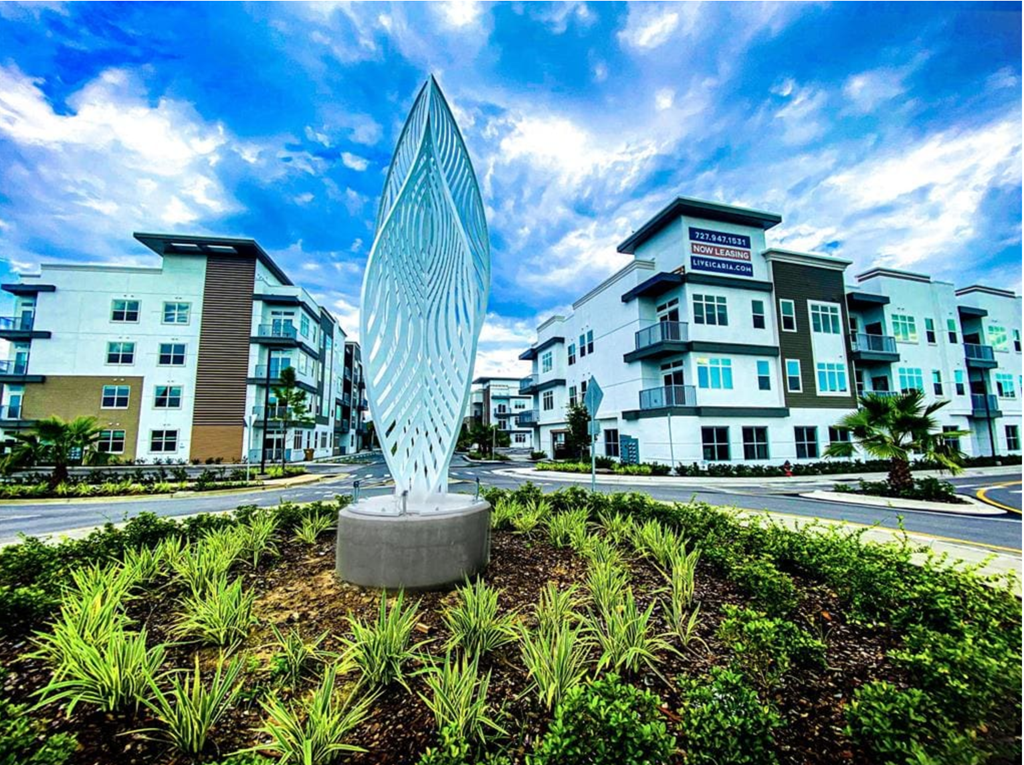 a statue in the middle of a garden in front of some apartment buildings