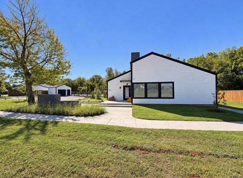 A modern white house with a black roof and a black chimney is surrounded by a green lawn and trees.