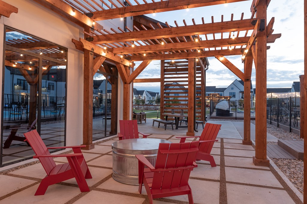 A wooden pergola with red chairs and a table is set up outside.