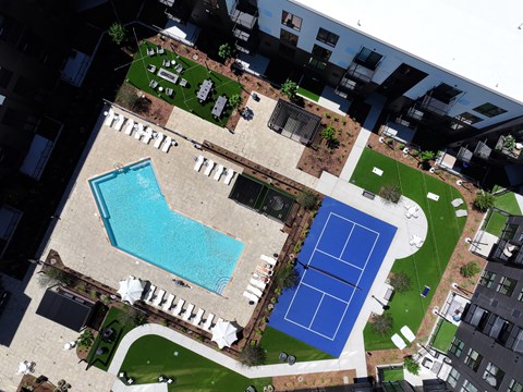 A pool and tennis court are surrounded by buildings.