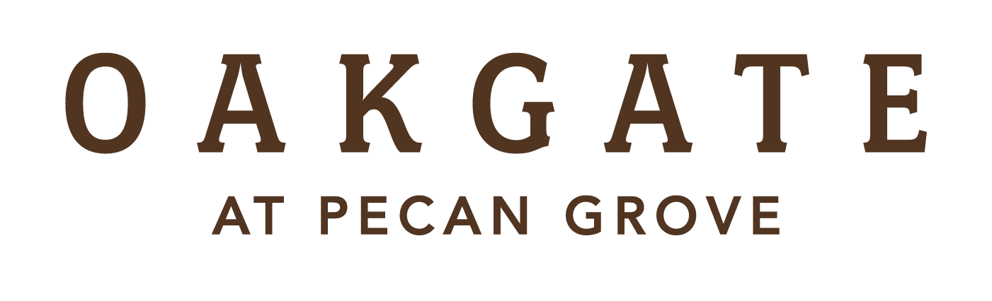 The image displays the text "OAKGATE AT PECAN GROVE" in large, brown letters on a black background.