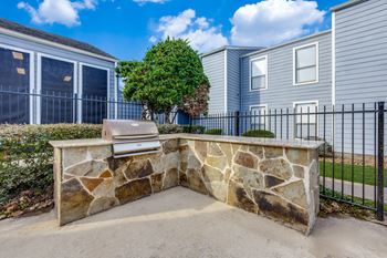 A stone bench with a wooden slat back is in front of a black fence and a green tree.