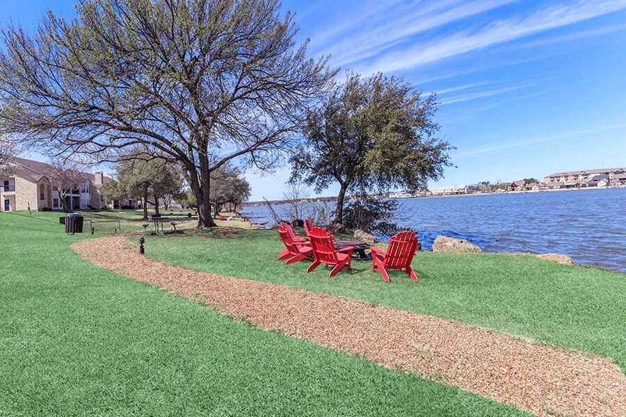 A lawn with a red chair and a table is in front of a body of water.