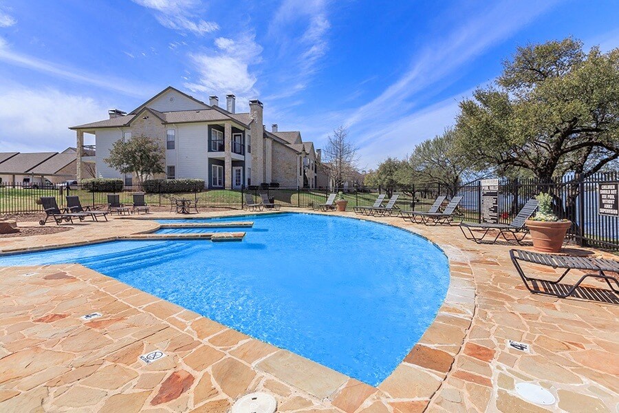 A large swimming pool surrounded by a stone patio and a house in the background.