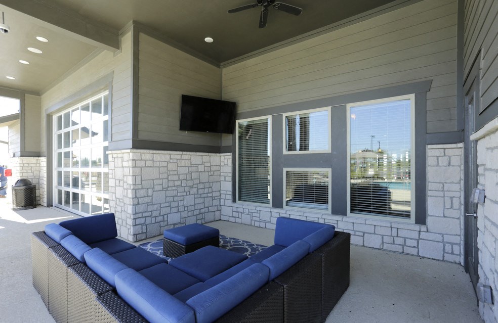 A patio with a blue couch and a television on the wall.