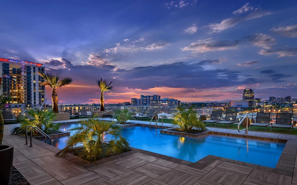A rooftop pool with palm trees and a city skyline at dusk.
