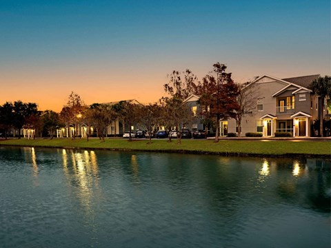A serene lake reflects the lights of a residential area at dusk.