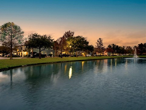 A serene park with a lake, trees, and a fountain at dusk.