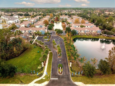A road with a roundabout in the middle of a grassy area with a lake and houses in the background.