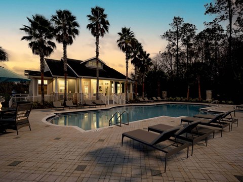 A poolside area with lounge chairs and a house with palm trees.