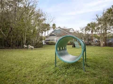 A green slide in a grassy area with trees and a house in the background.