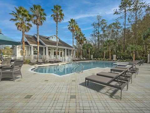 A pool surrounded by lounge chairs and palm trees.