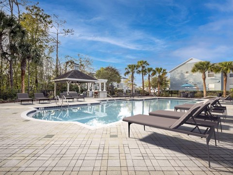 A pool with a gazebo and lounge chairs.