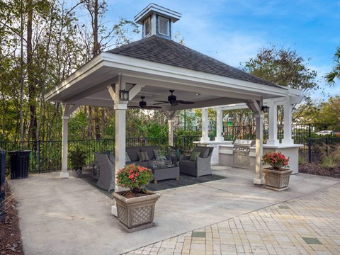A gazebo with a black roof and white pillars is surrounded by a black fence and has a fan on top.