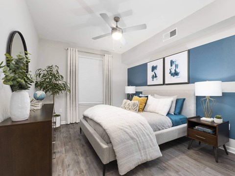 A bedroom with a bed, nightstand, and a plant.