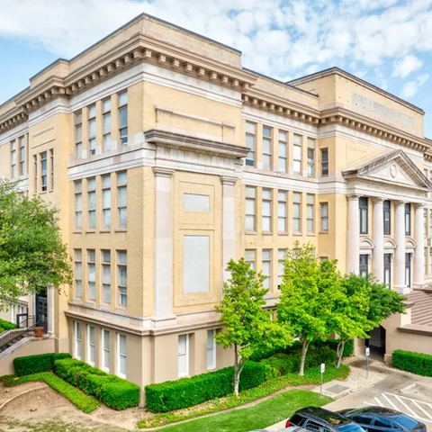 A large, beige building with a classical design and a green lawn in front.