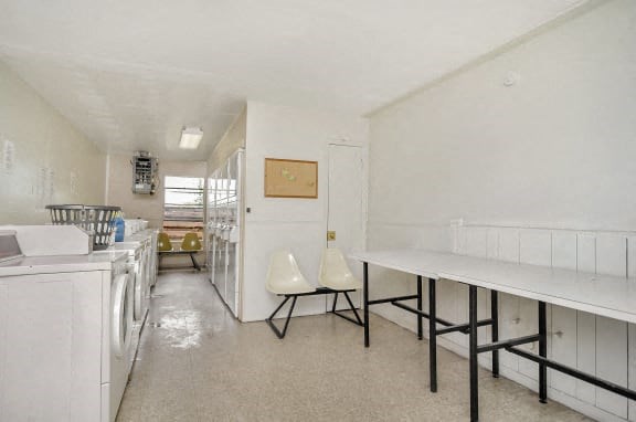 A laundry room with a white washer and dryer, a white chair, and a white table.