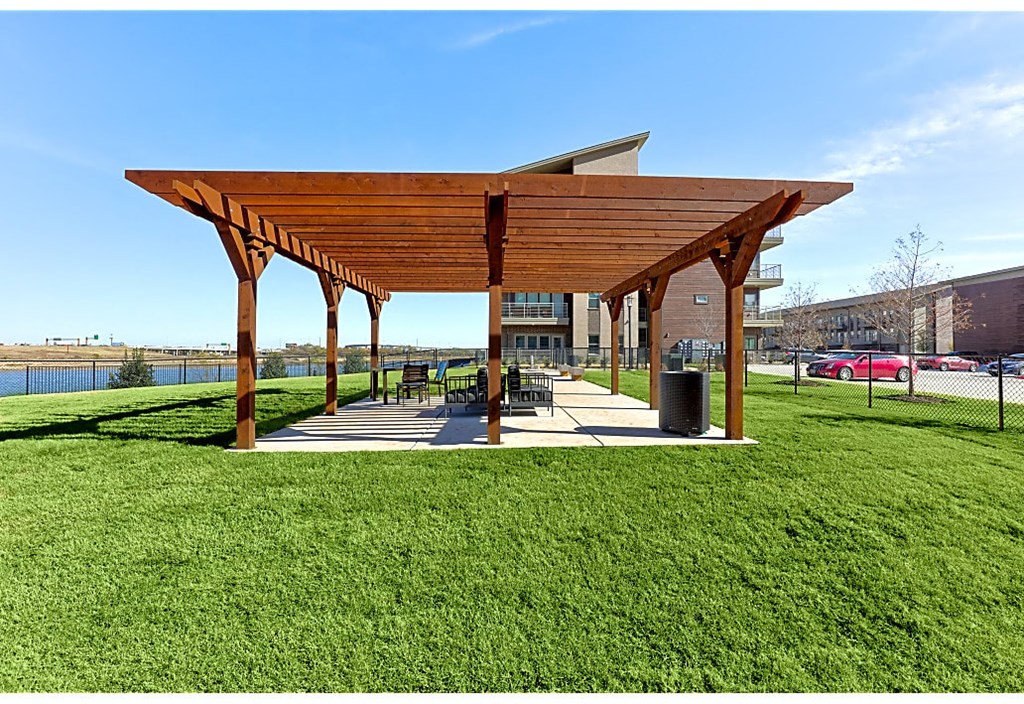 A wooden pavilion with a grassy area in front is shown.