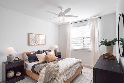 a carpeted bedroom with queen size bed, dresser, ceiling fan, and large window