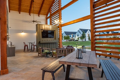 A wooden table with benches and a television in a covered outdoor area.