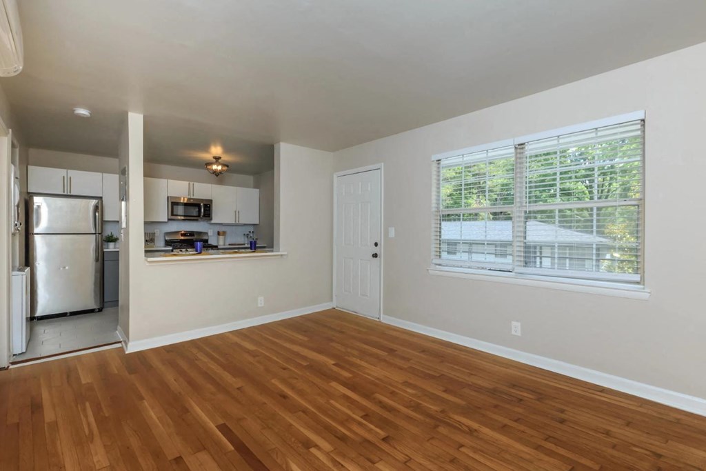 an empty living room with a kitchen in the background