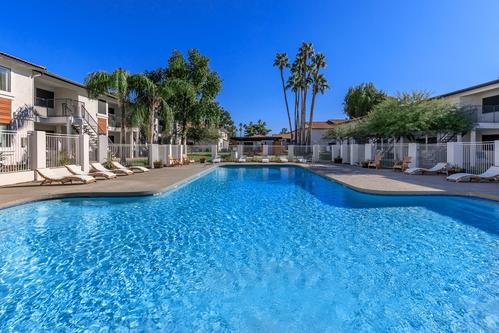 a large blue pool with chaise lounge chairs and palm trees in the background