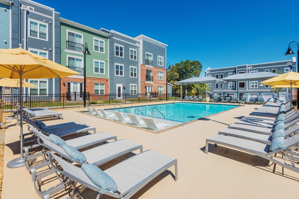 A pool area with sun loungers and umbrellas in front of apartment buildings.