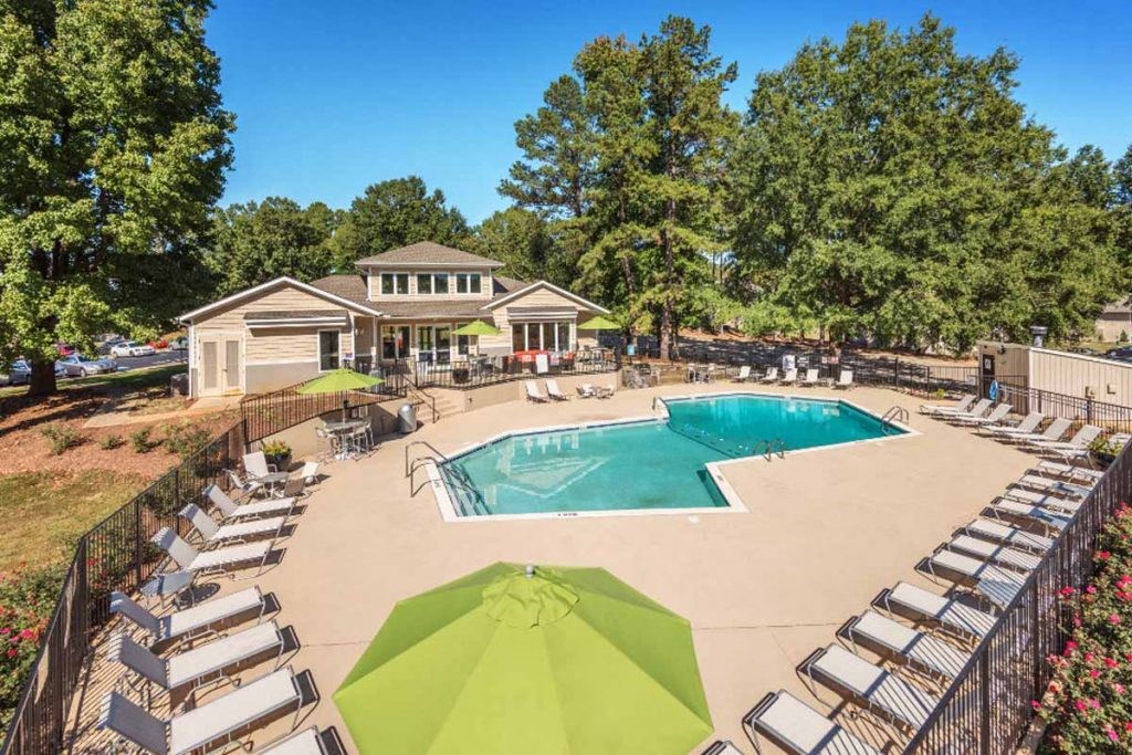 a pool with lounge chairs and umbrellas in front of a house