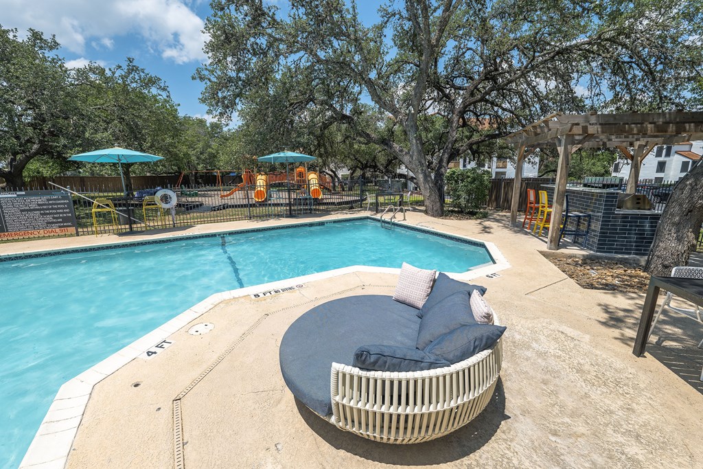 A round wicker lounge chair with a blue cushion sits on the edge of a pool.