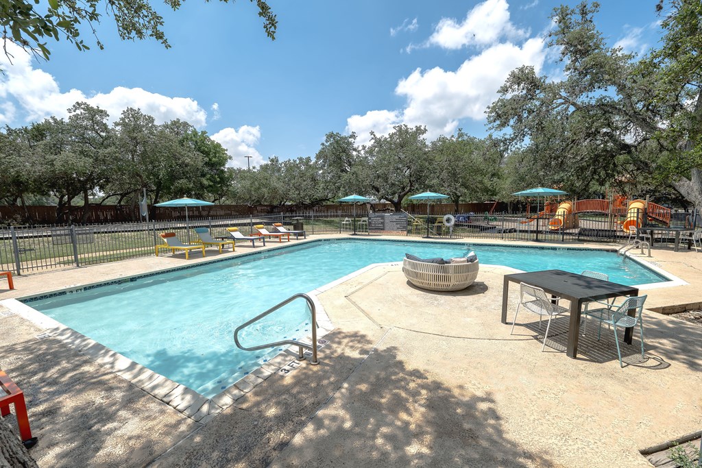 A large outdoor swimming pool surrounded by trees and a fence.