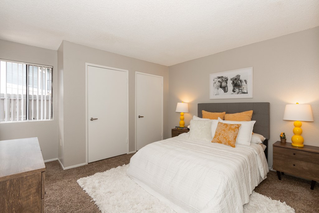 A bedroom with a large bed, two nightstands with lamps, and a window with blinds.