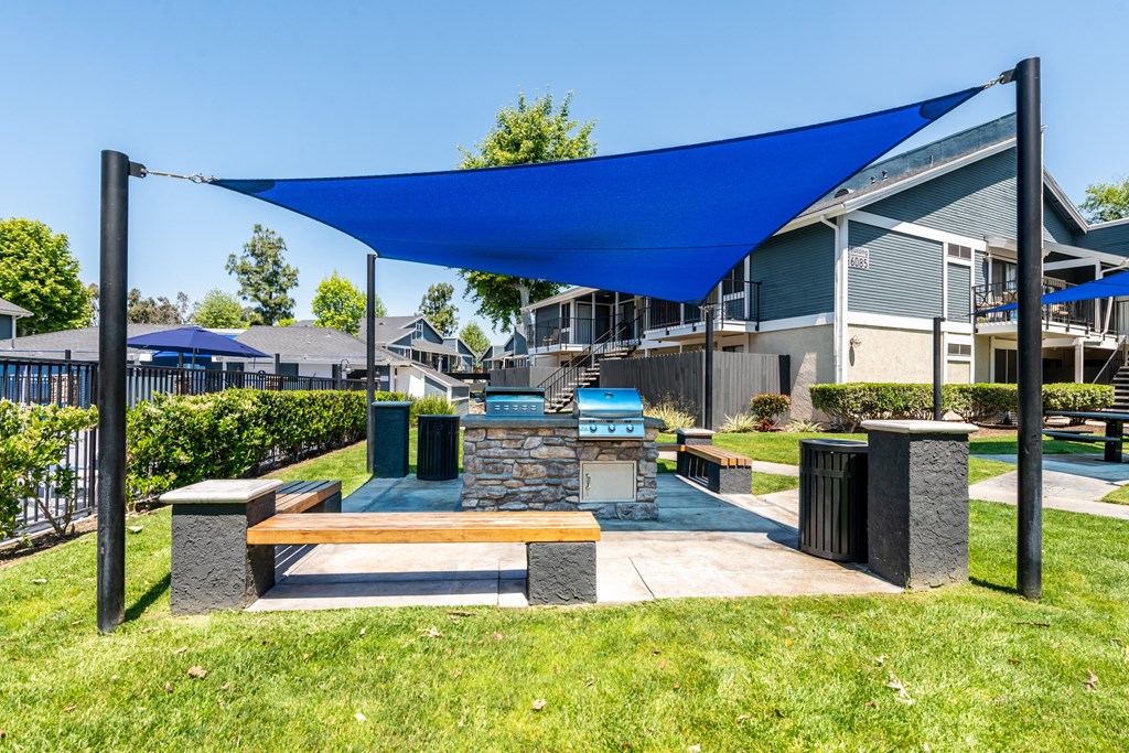A blue shade structure is over a bench in a grassy area.