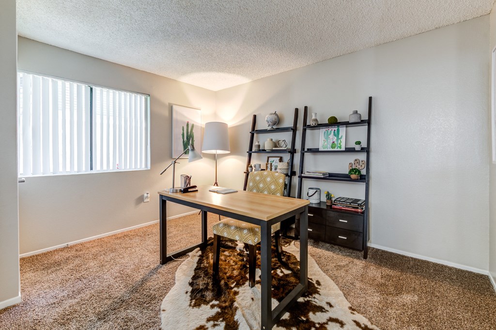 A room with a desk, chair, and shelves with various items.