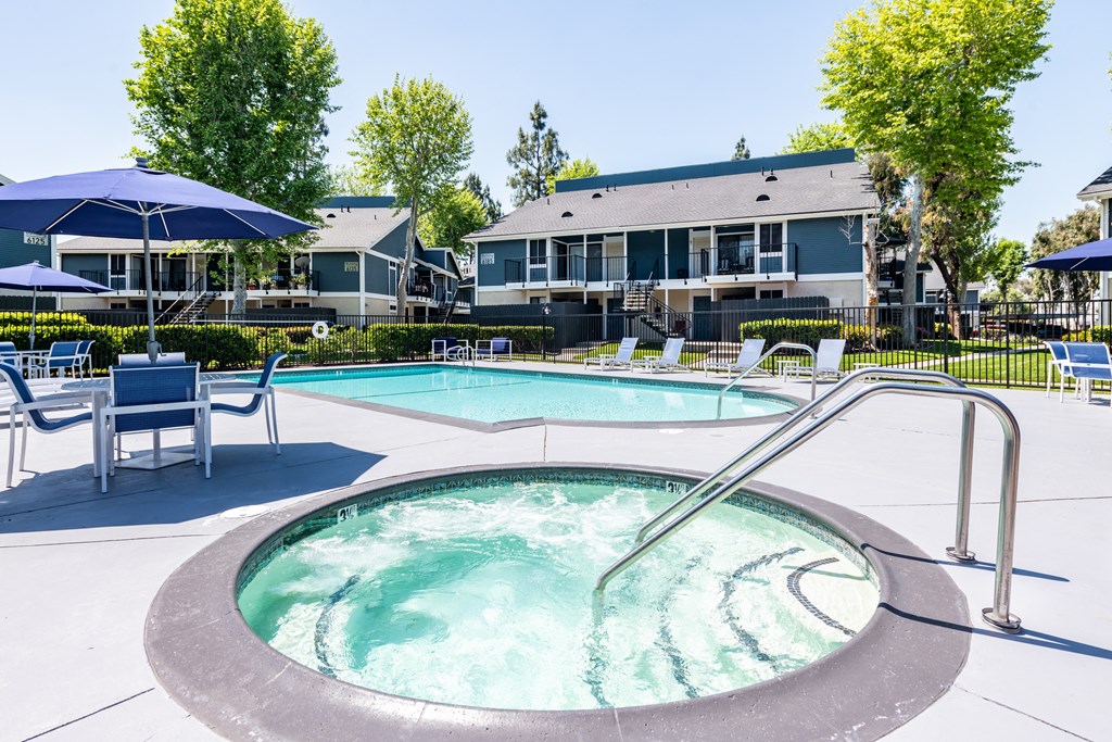 A hot tub sits in the middle of a pool surrounded by chairs and umbrellas.