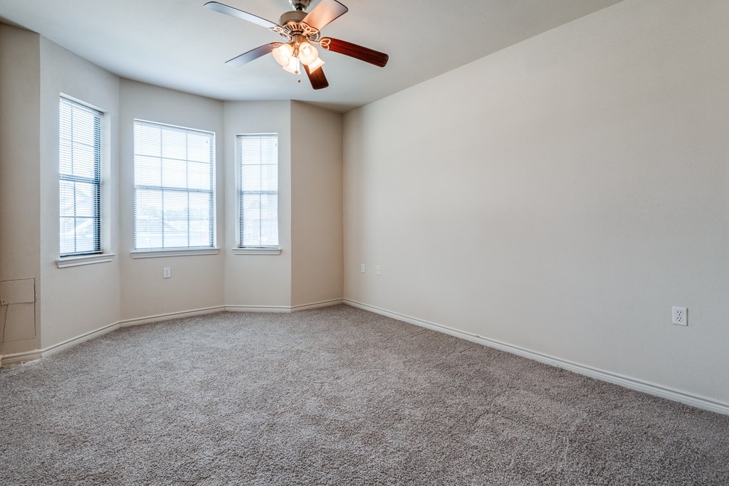 an empty room with a ceiling fan and three windows